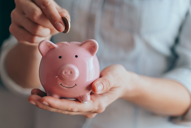 female hands hold a pink piggy bank and puts a coin there