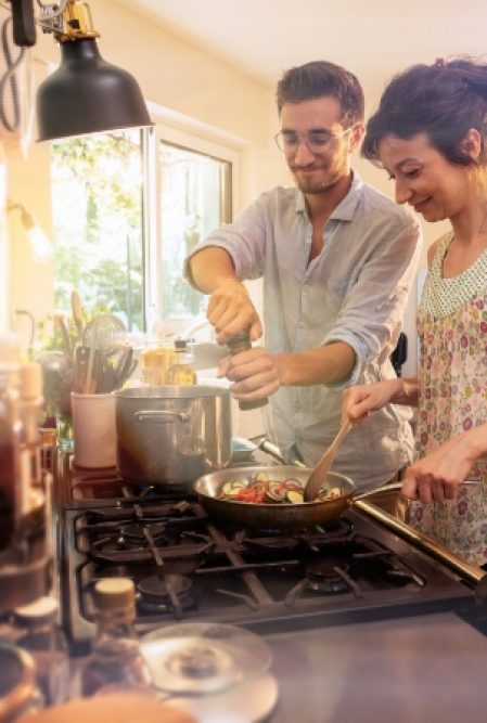 two people cook over a stove while friends mingle in the background